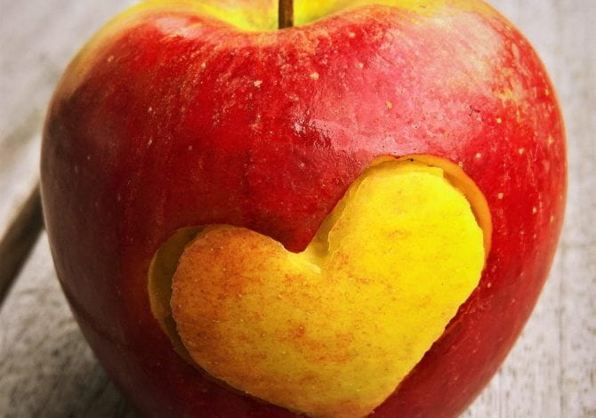 Student Services - A red apple on a bench with a heart shape cur out of it.
