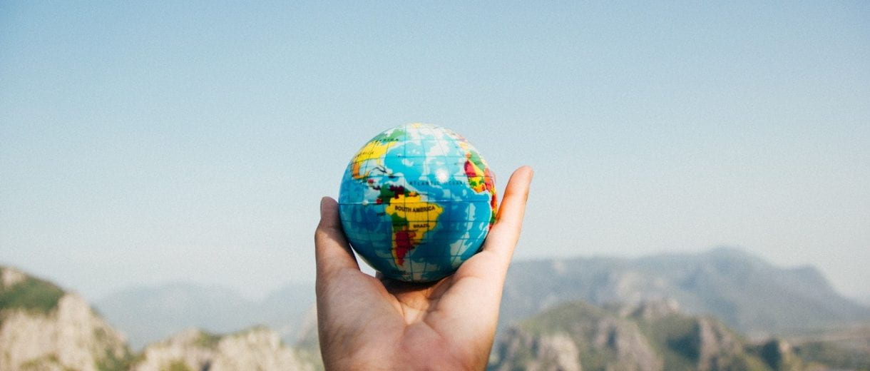 Student Services - A hand holding a miniature globe in front of a landscape.
